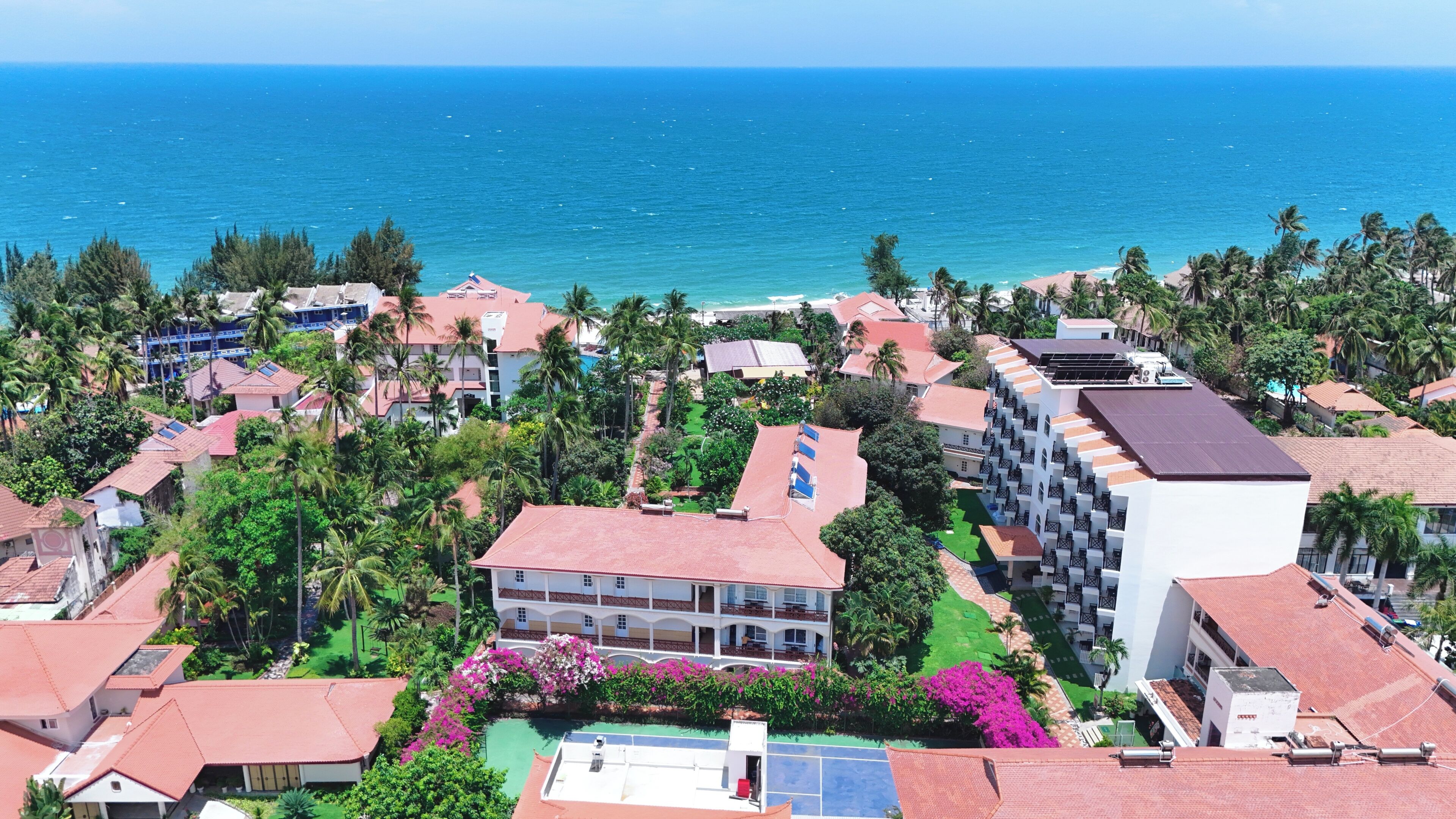 A coastal residential area with houses, a large building with balconies, and a view of the ocean.