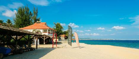 Una spiaggia con una struttura a tetto di paglia, sedie a sdraio e una bandiera.