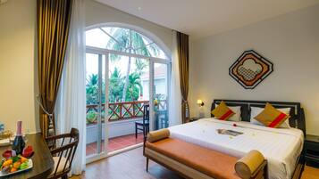 Habitación de hotel con cama, mesa de comedor con sillas, balcón con vista a palmeras y un adorno decorativo en la pared.
