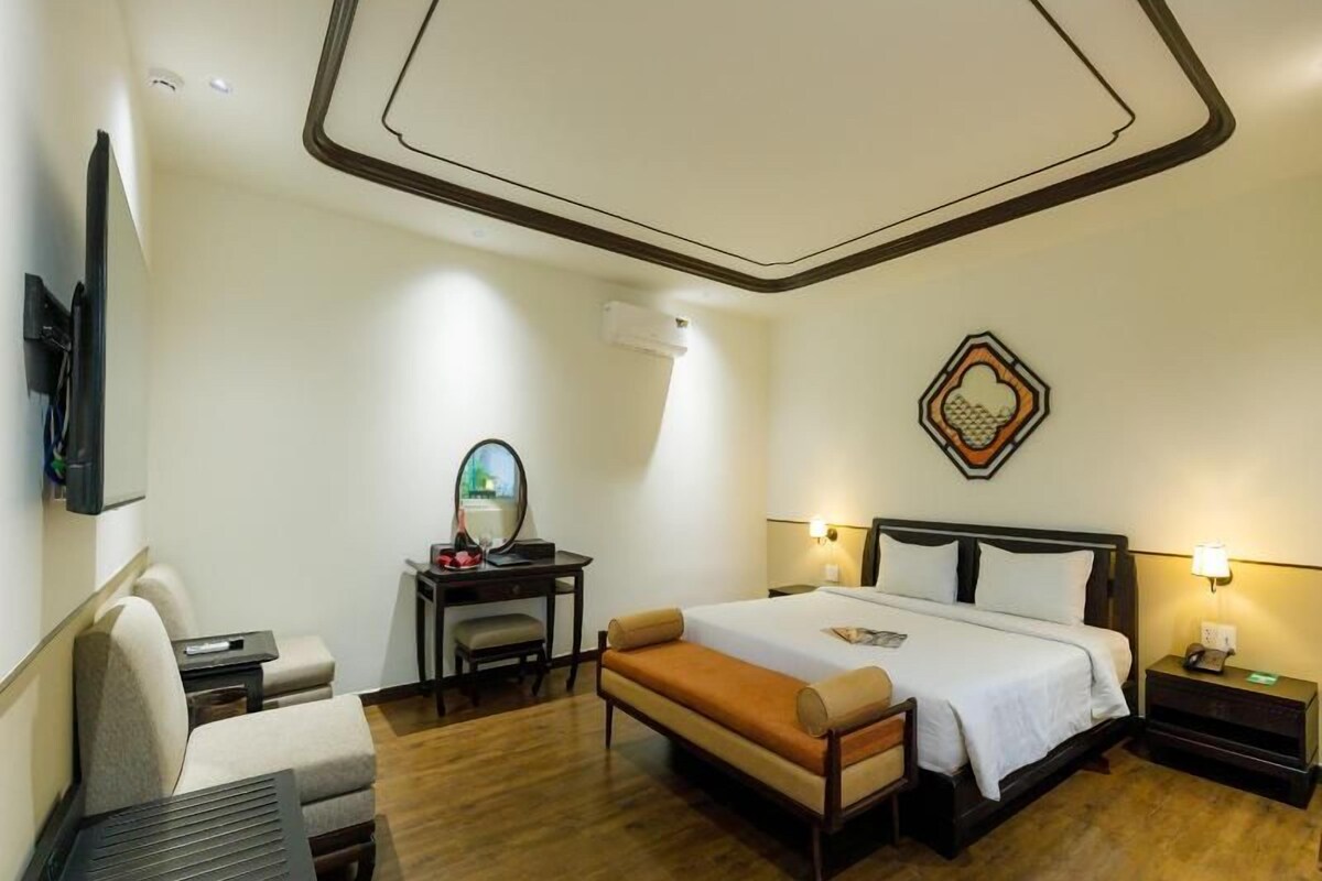 Une chambre d’hôtel comprenant un lit, des tables de chevet, un bureau, une chaise, un miroir et un téléviseur fixé au mur.