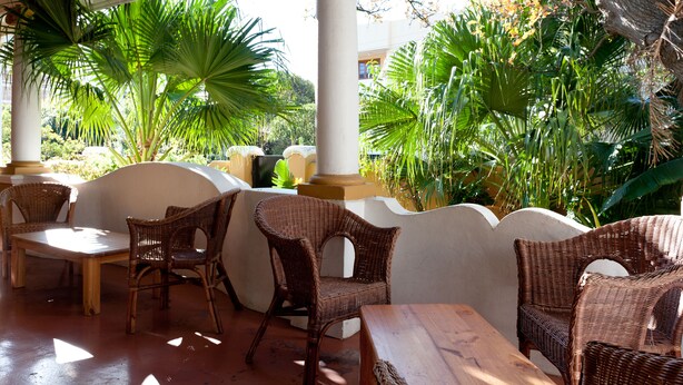 Un área de estar al aire libre techada con muebles de mimbre y vista a exuberante follaje.