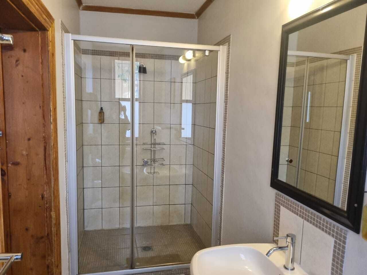 A bathroom with a glass-enclosed shower, a sink, and a mirror.