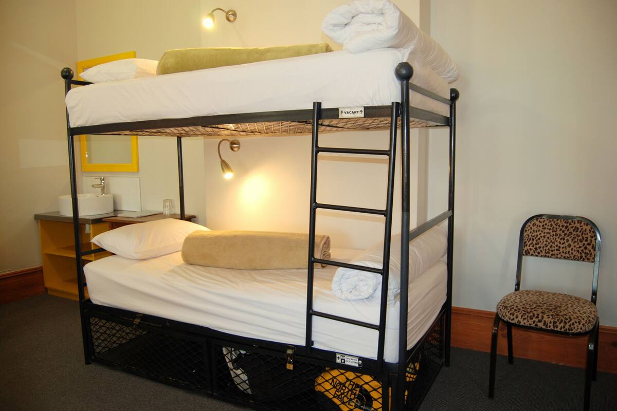 Een stapelbed met een spiegel, een stoel en een klein bureau met een lamp.
