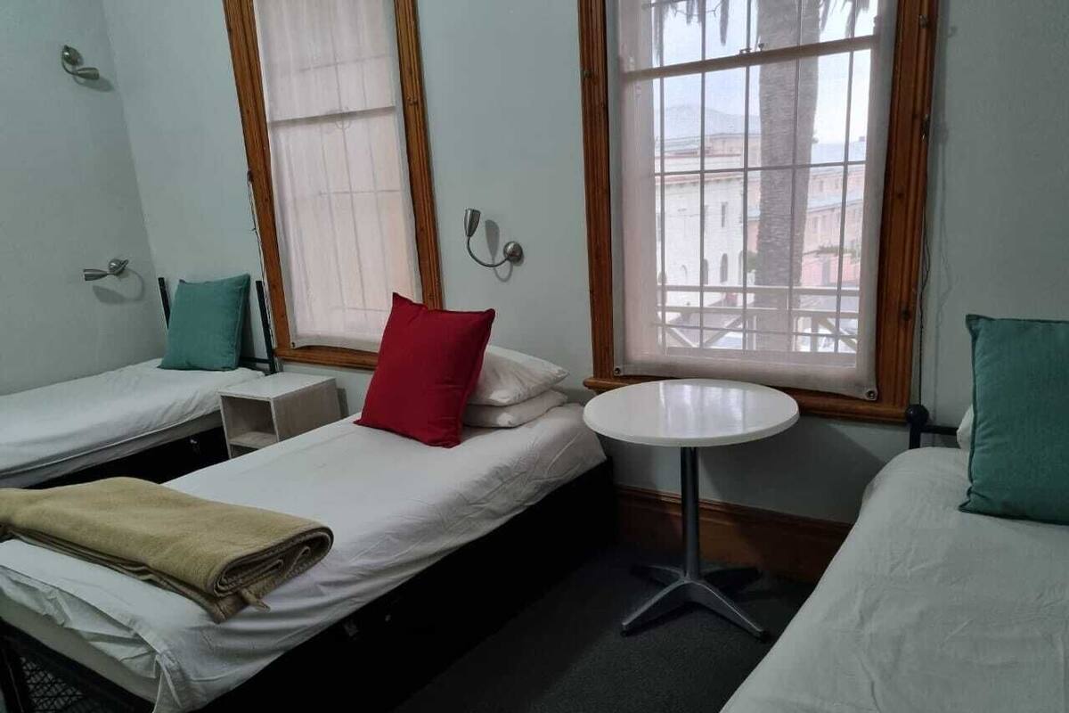 Een kamer met twee enkele bedden, een klein rond tafeltje en een raam met uitzicht op gebouwen.
