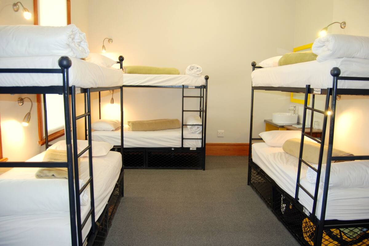 Een kamer met vier stapelbedden, elk voorzien van witte lakens en een klein nachtkastje.