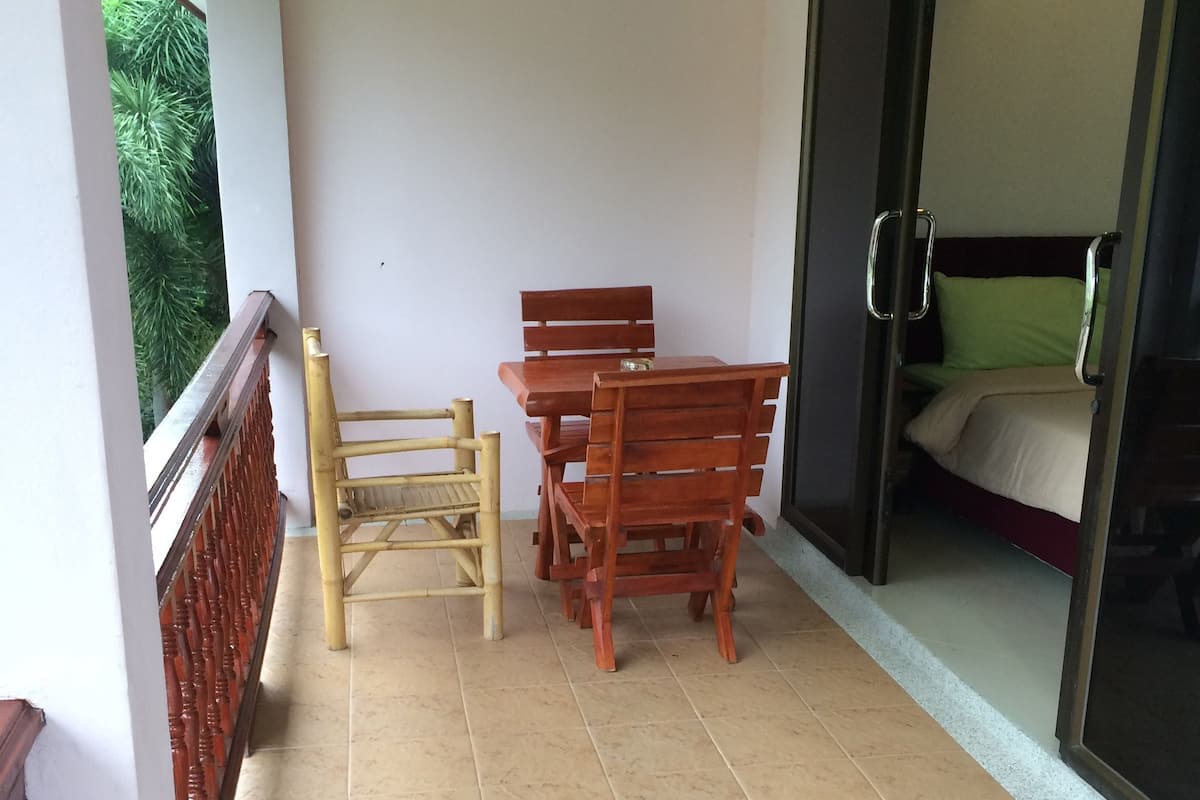 Un balcón con mesa y sillas, una puerta corrediza que da a un dormitorio y vista a zonas verdes.
