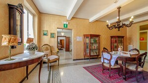 Um saguão de hotel com balcão de recepção, um candelabro, uma biblioteca e um espaço de refeições.