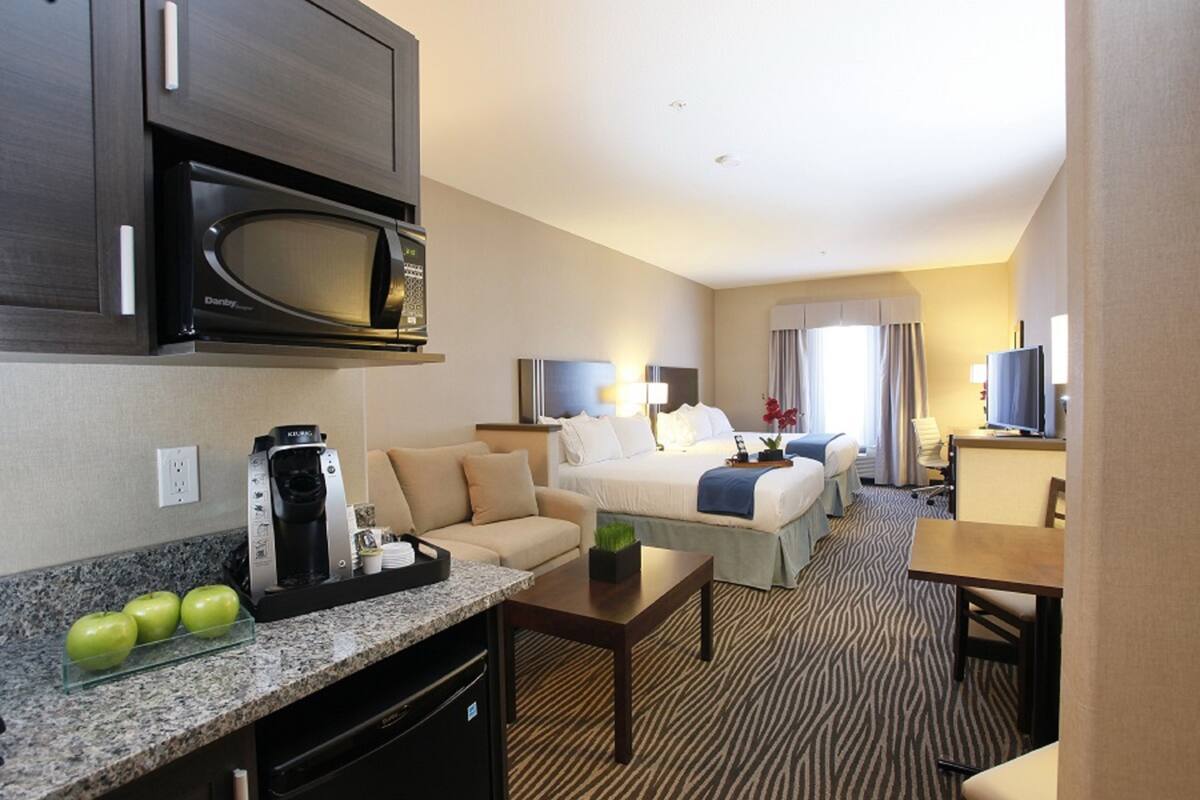 A hotel room with a kitchenette, a bed, a sofa, a dining table, and a television.