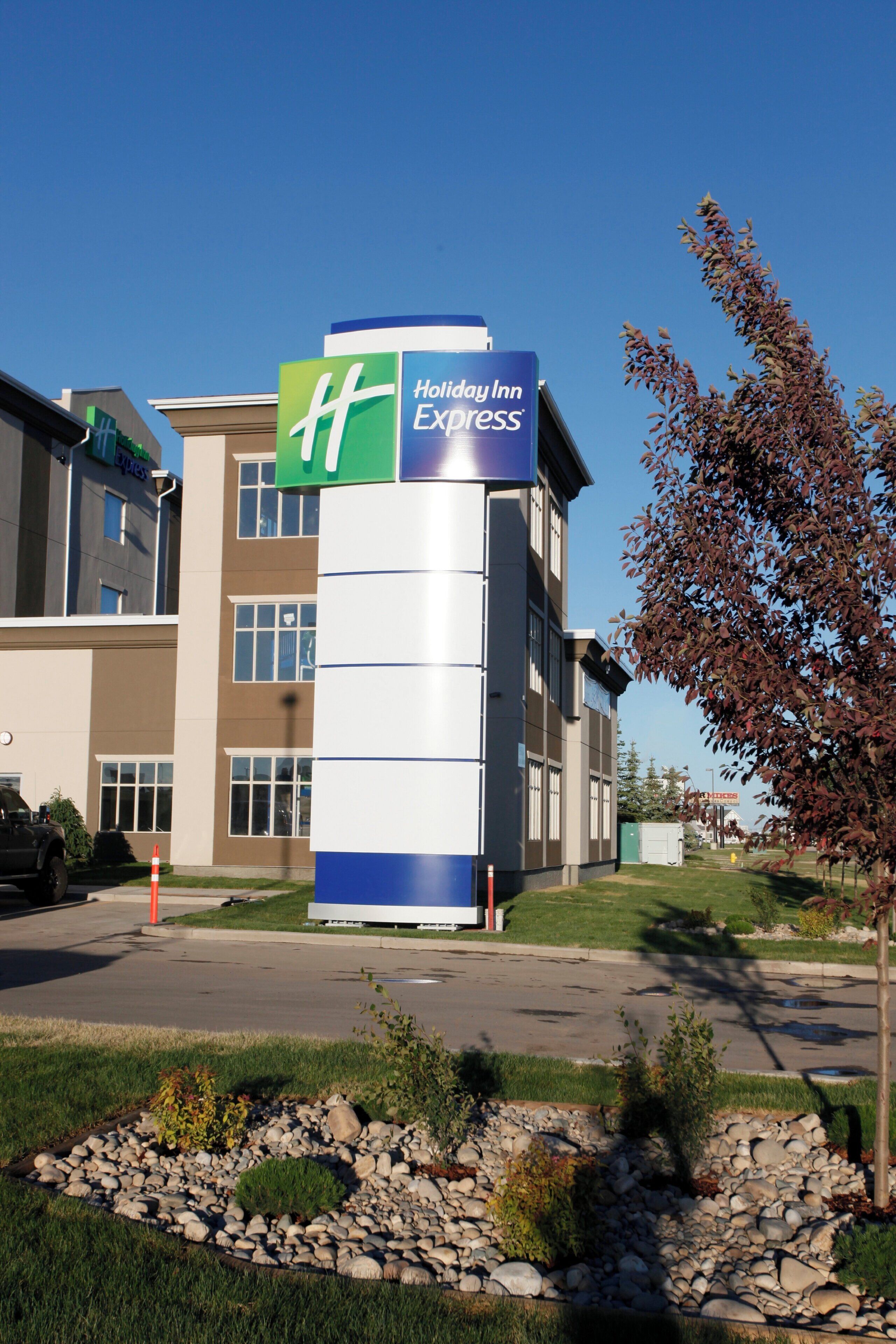 Un bâtiment de l'hôtel Holiday Inn Express, avec une enseigne bien visible, un parking et un espace paysager agrémenté de rochers et d'arbustes.