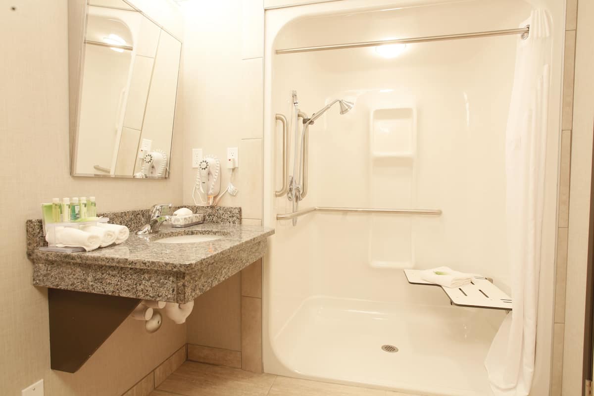 A bathroom with a granite countertop sink, a mirror, a shower with a glass door, and a towel rack.