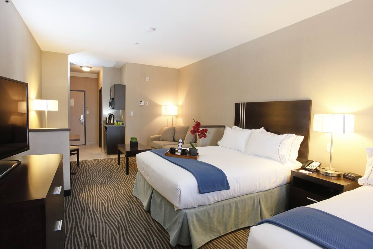 A hotel room with a large bed, a desk, a chair, a TV, and a kitchenette.