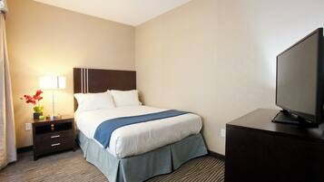 A hotel room with a bed, a desk, a television, and a nightstand with a lamp and flowers.