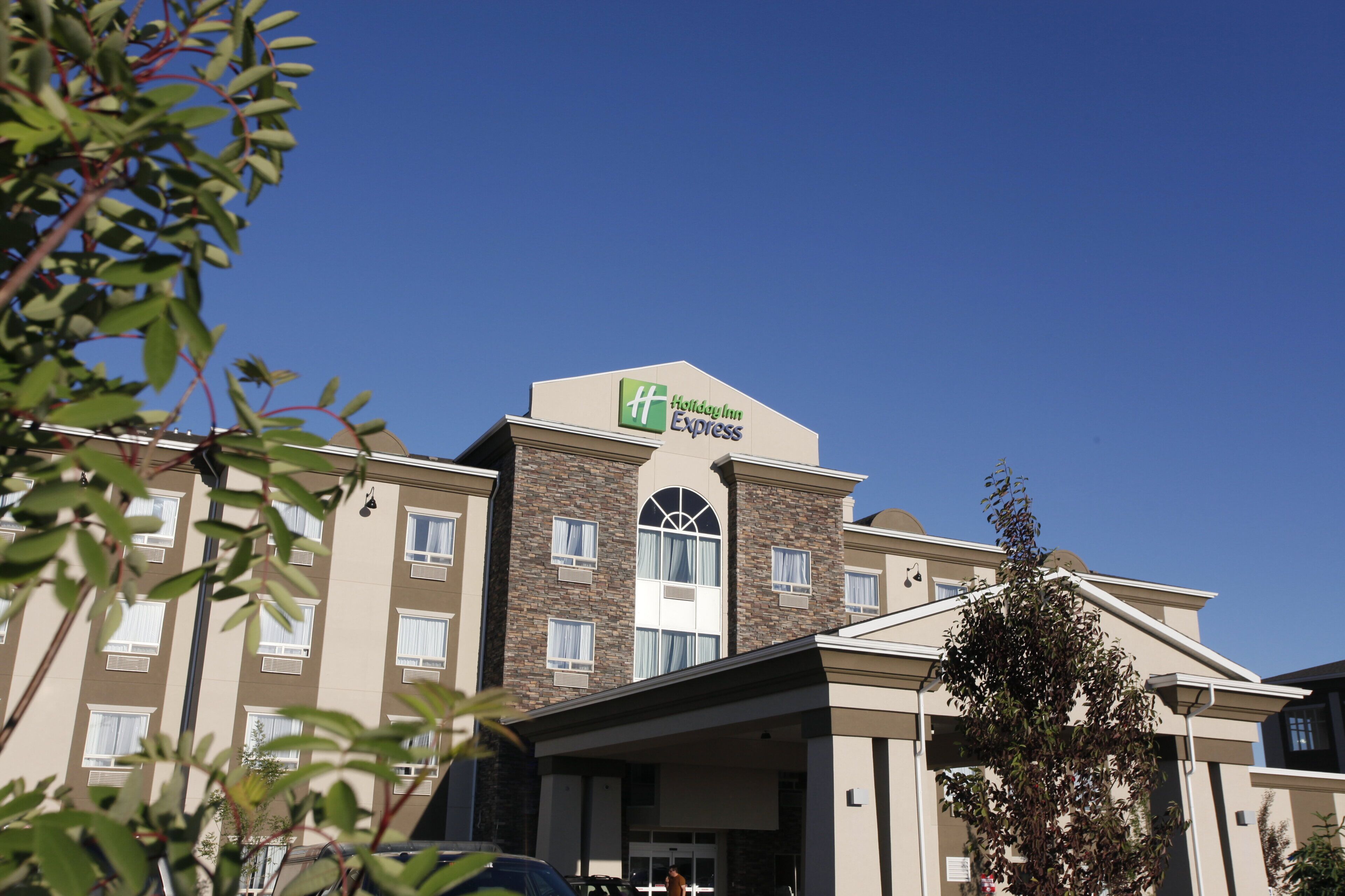 Un hotel Holiday Inn Express con un diseño moderno, que cuenta con un letrero llamativo en el techo y una entrada cubierta.