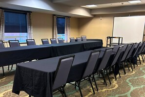Un salón de conferencias con una larga mesa, sillas, una pantalla de proyector y piso alfombrado.
