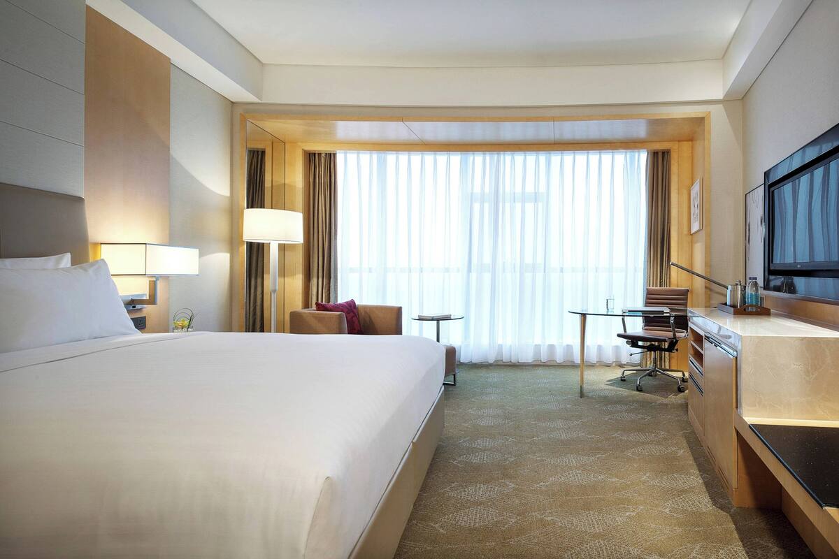 Habitación de hotel con una cama grande, un escritorio, una silla, un televisor y una ventana con cortinas.