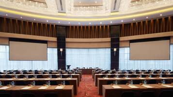 A conference room with rows of tables, chairs, and a large screen at the front.