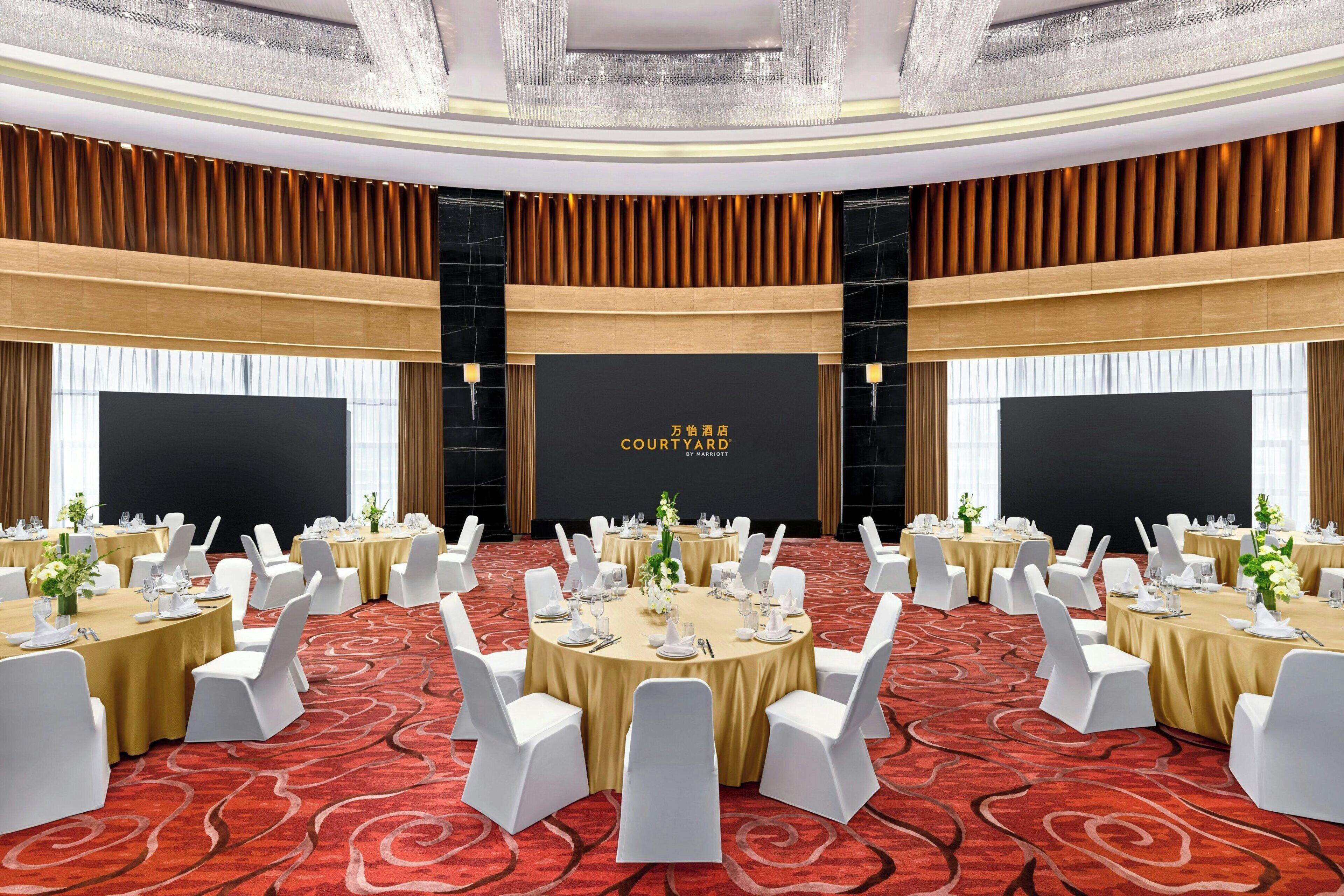 A conference room with round tables, white chairs, and a black backdrop with text.