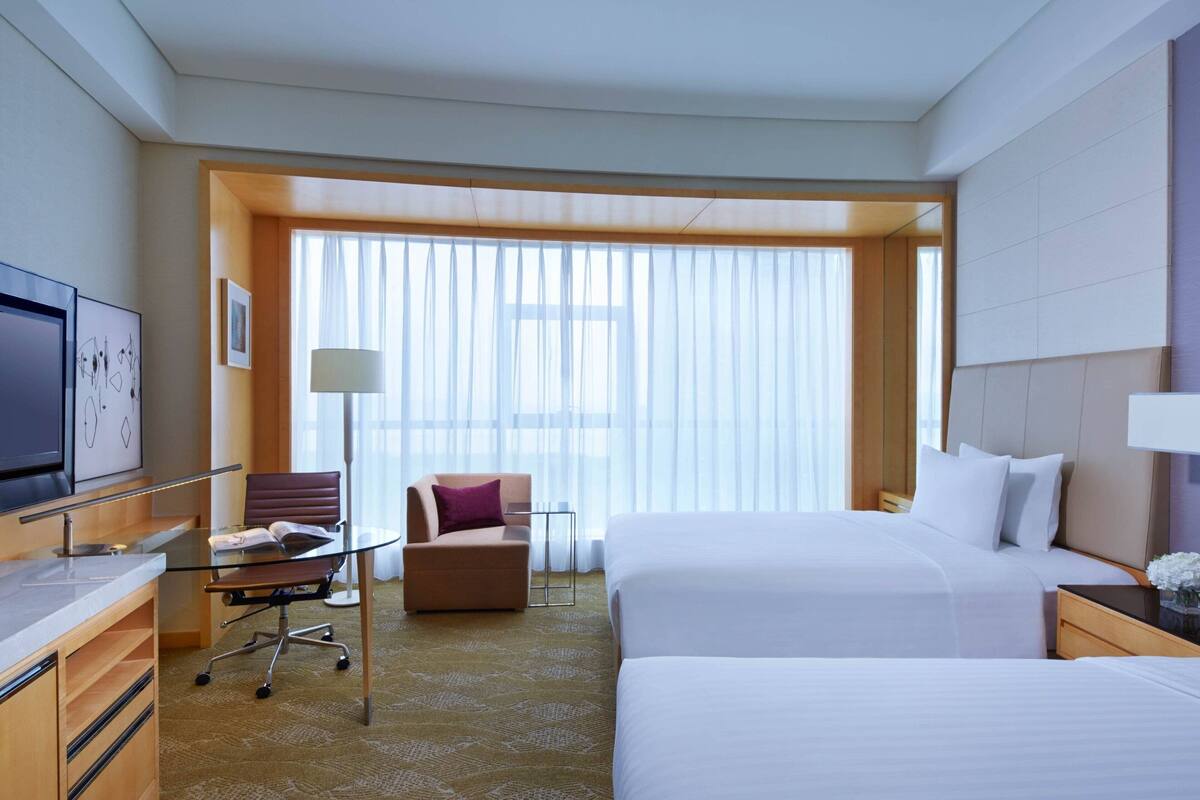 Habitación de hotel con dos camas, un escritorio, una silla y una televisión.