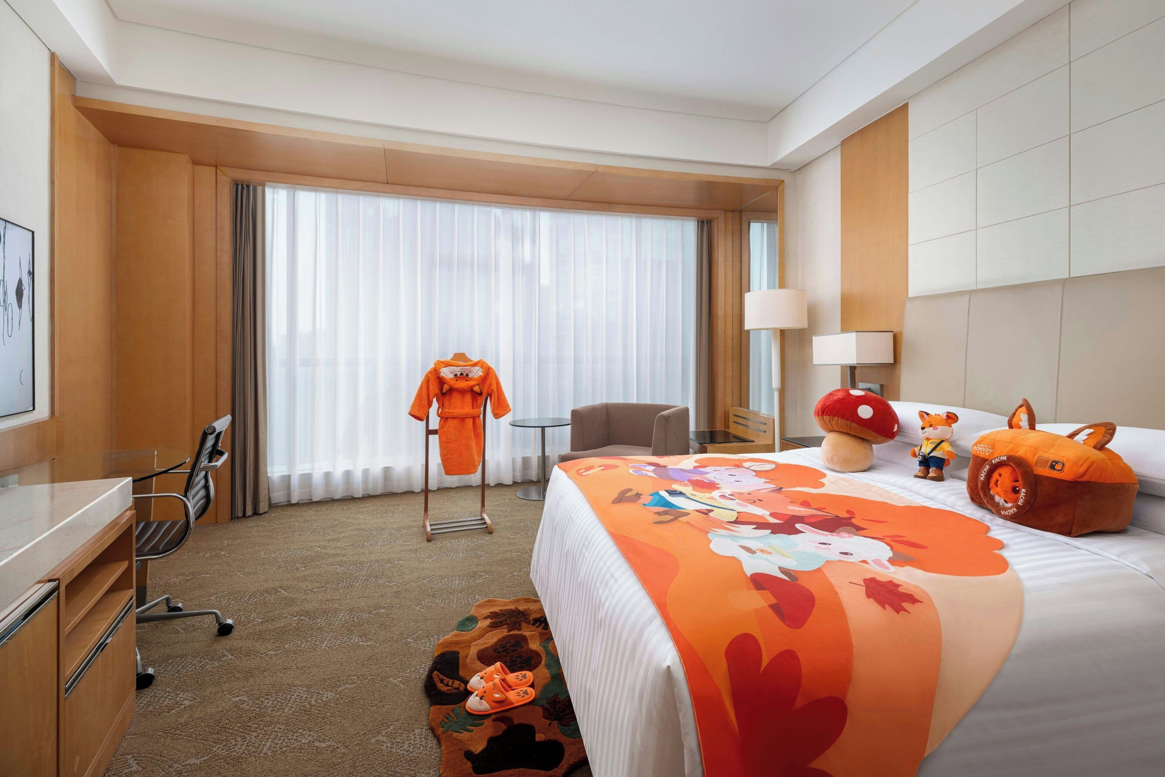 A hotel room with a bed, a desk, a chair, a lamp, and a window with curtains.