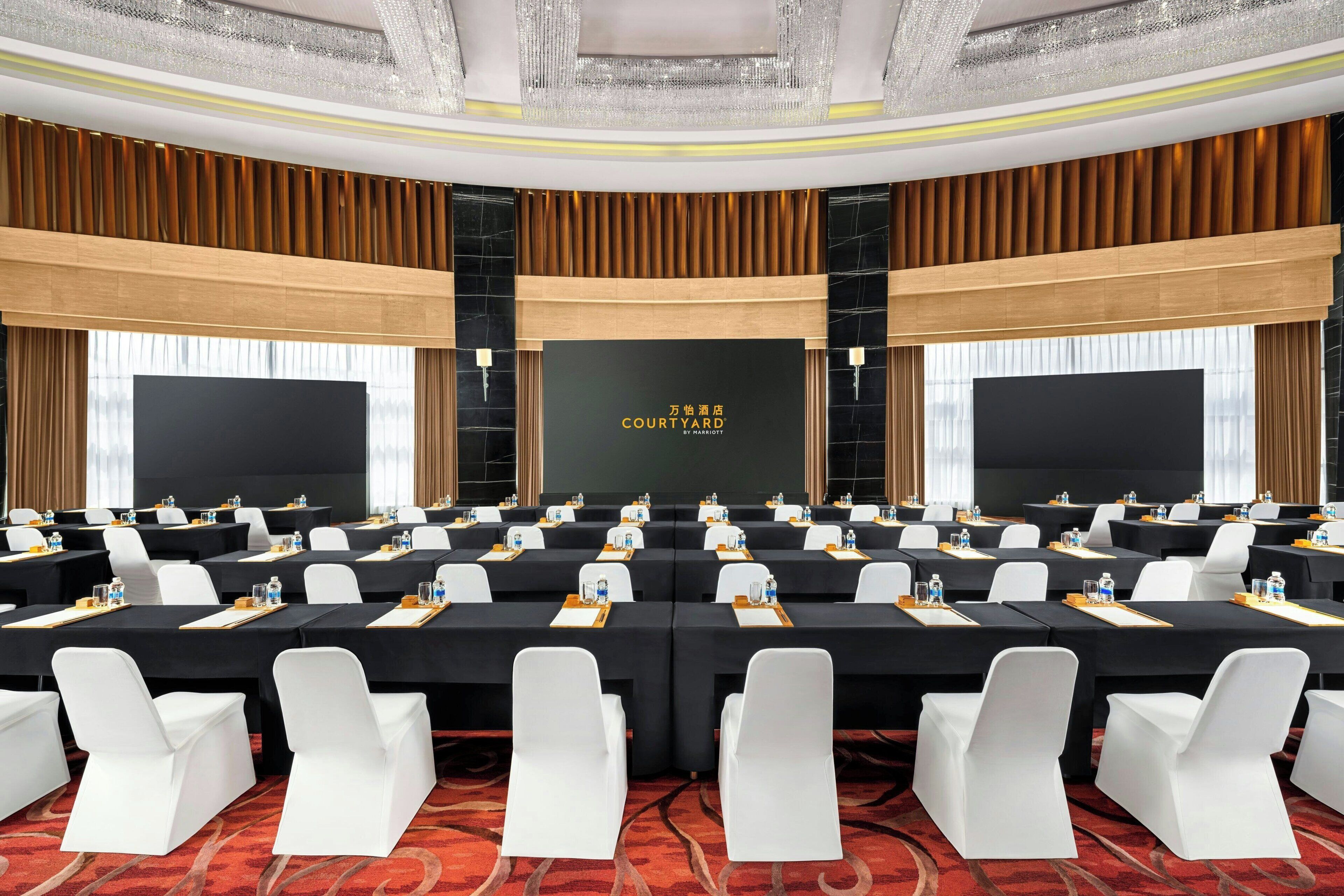 A conference room with a long table, white chairs, and a black backdrop with text.