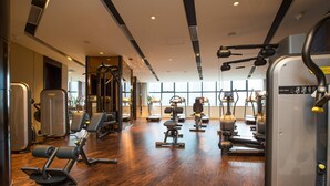 Ein Fitnessraum mit unterschiedlichen Trainingsgeräten, Holzboden und großen Fenstern für viel Tageslicht.