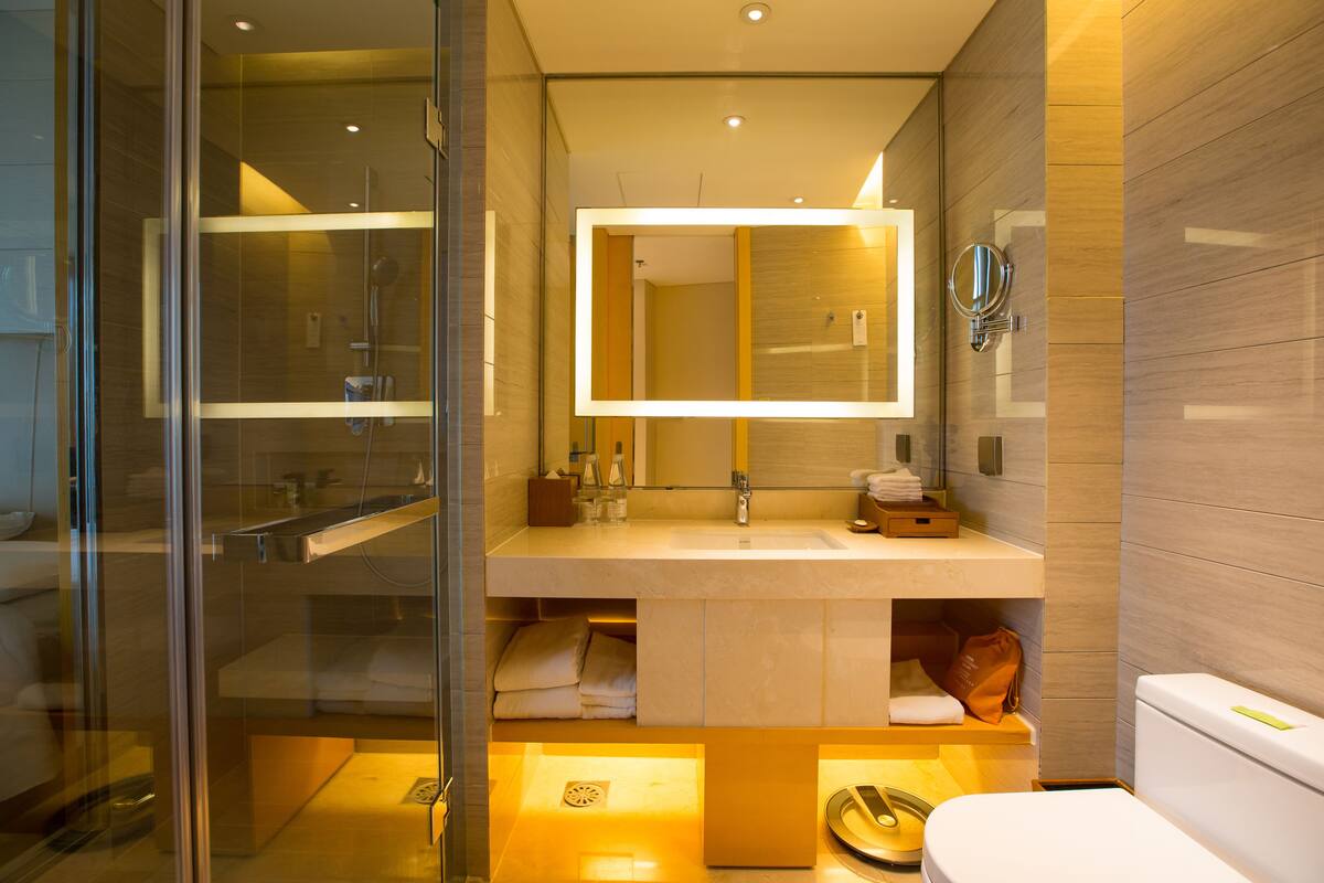 Un baño moderno con cabina de ducha de vidrio, un espejo grande y un inodoro blanco.