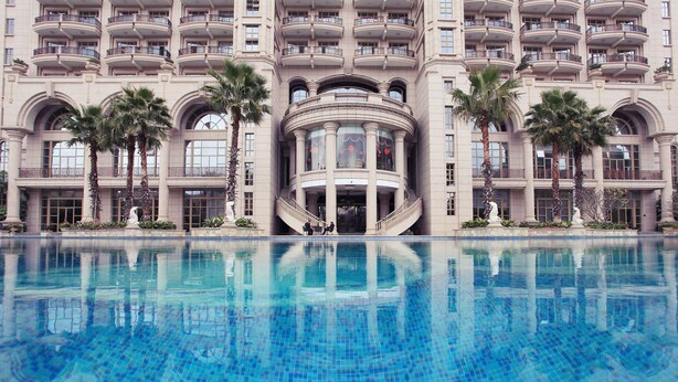A hotel with a large pool, multiple balconies, and palm trees.