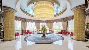 A grand lobby with a central round table, large columns, and red seating.