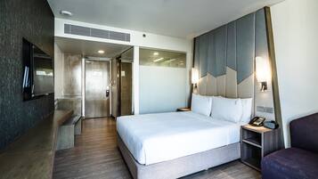 A modern hotel room with a large bed, a TV mounted on the wall, and a small desk with a lamp.