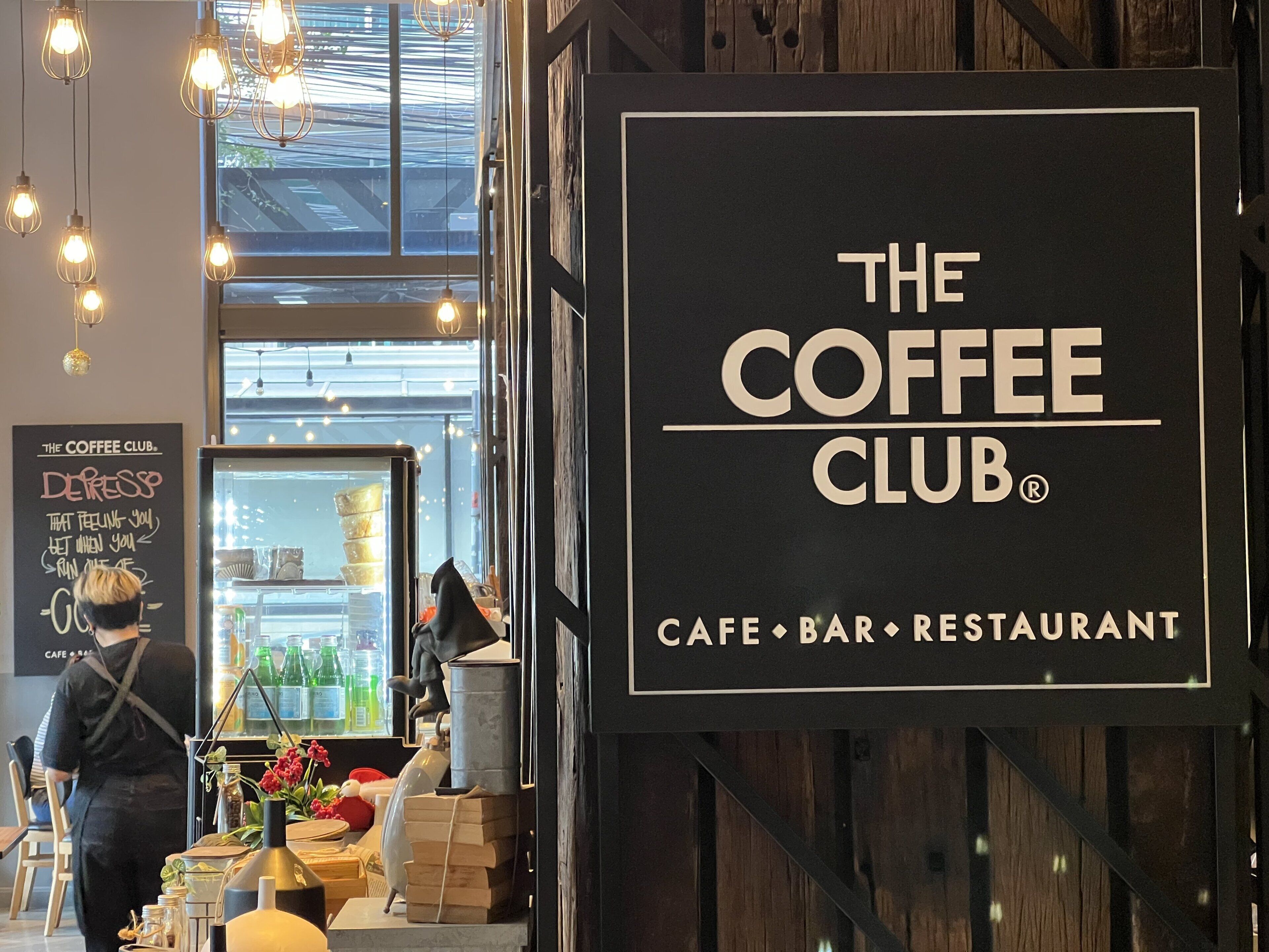 Een café interieur met een bord waarop 'The Coffee Club' staat en een menukaart.
