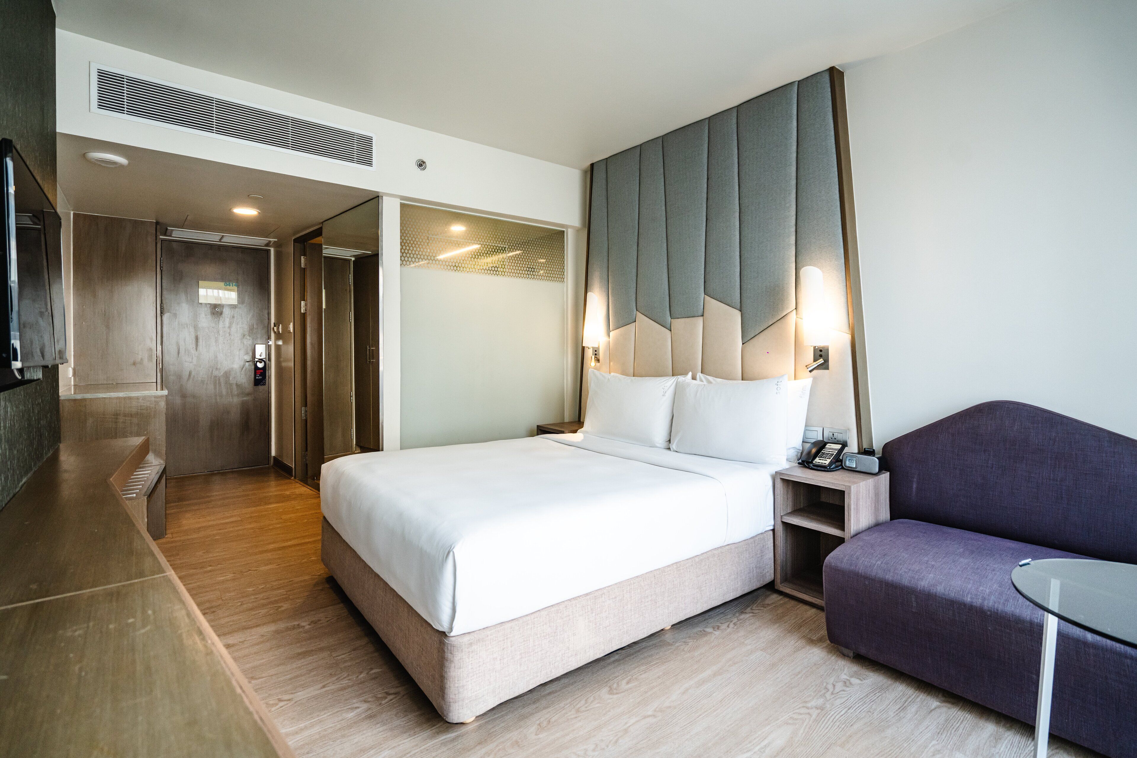 A modern hotel room with a large bed, a small sofa, a desk, and a walk-in closet.