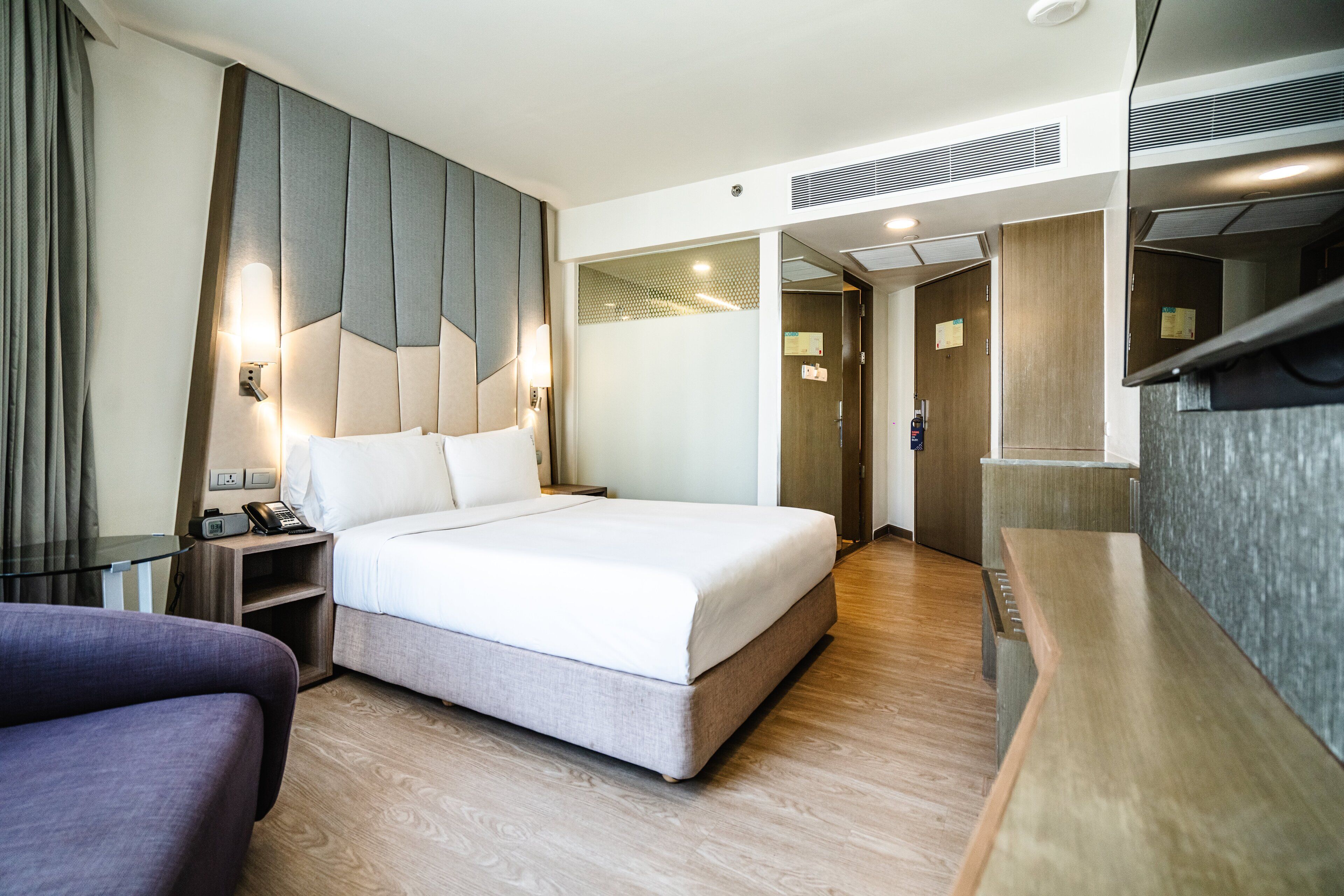 A modern hotel room with a large bed, bedside tables, a desk, and a seating area.