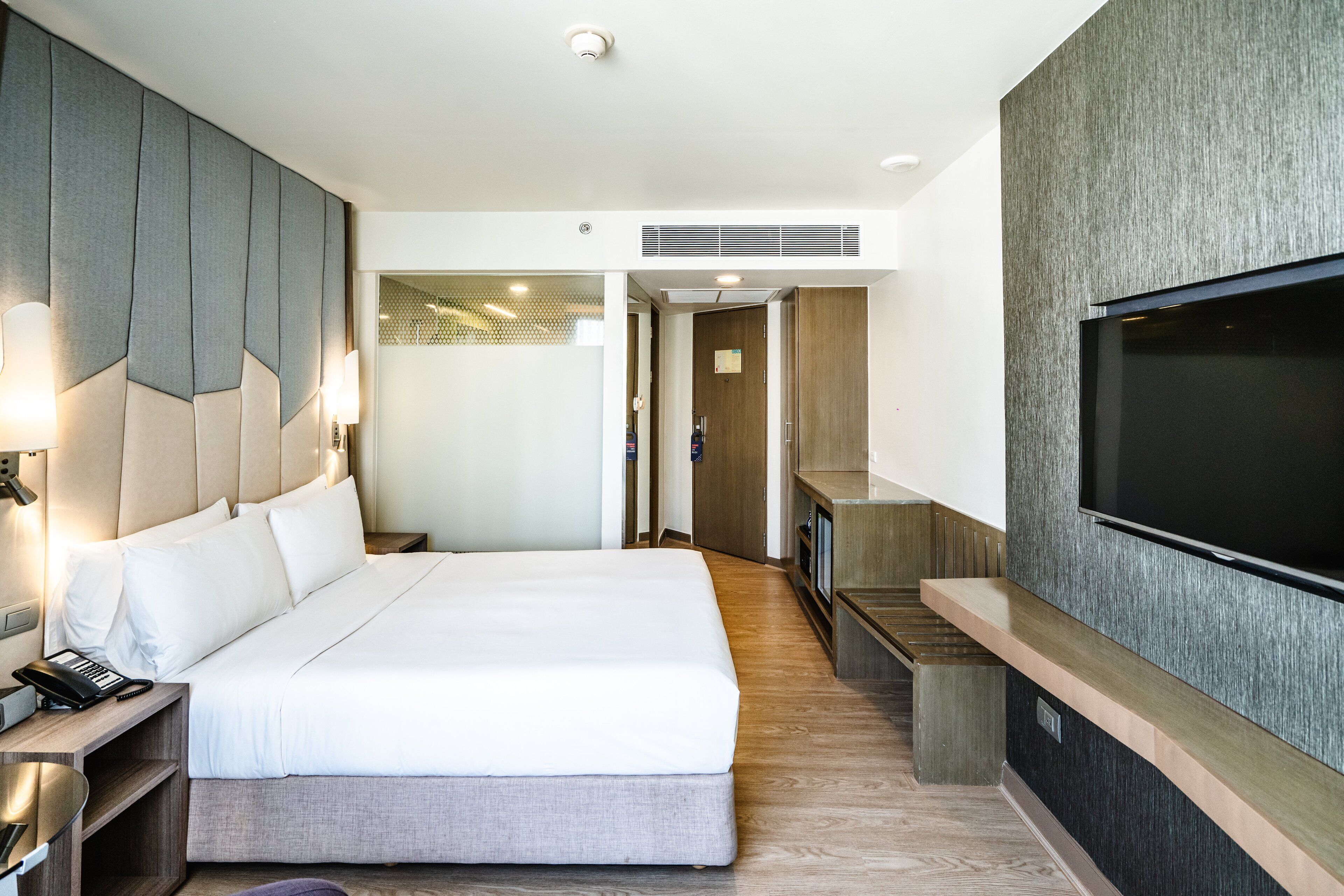 Una habitación de hotel moderna con una cama grande, un televisor montado en la pared y un escritorio con lámpara.