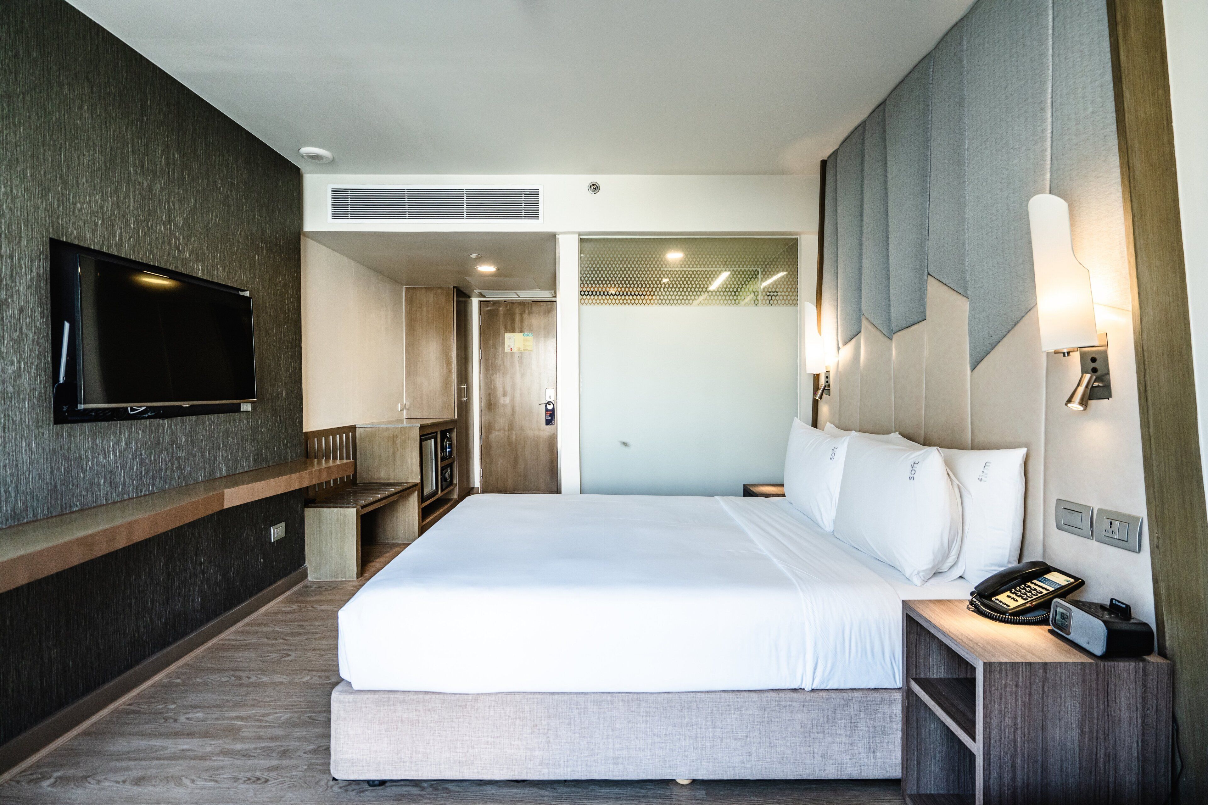 Habitación de hotel con una cama grande, un televisor de pantalla plana montado en la pared, una mesita de noche con teléfono y un pequeño escritorio.