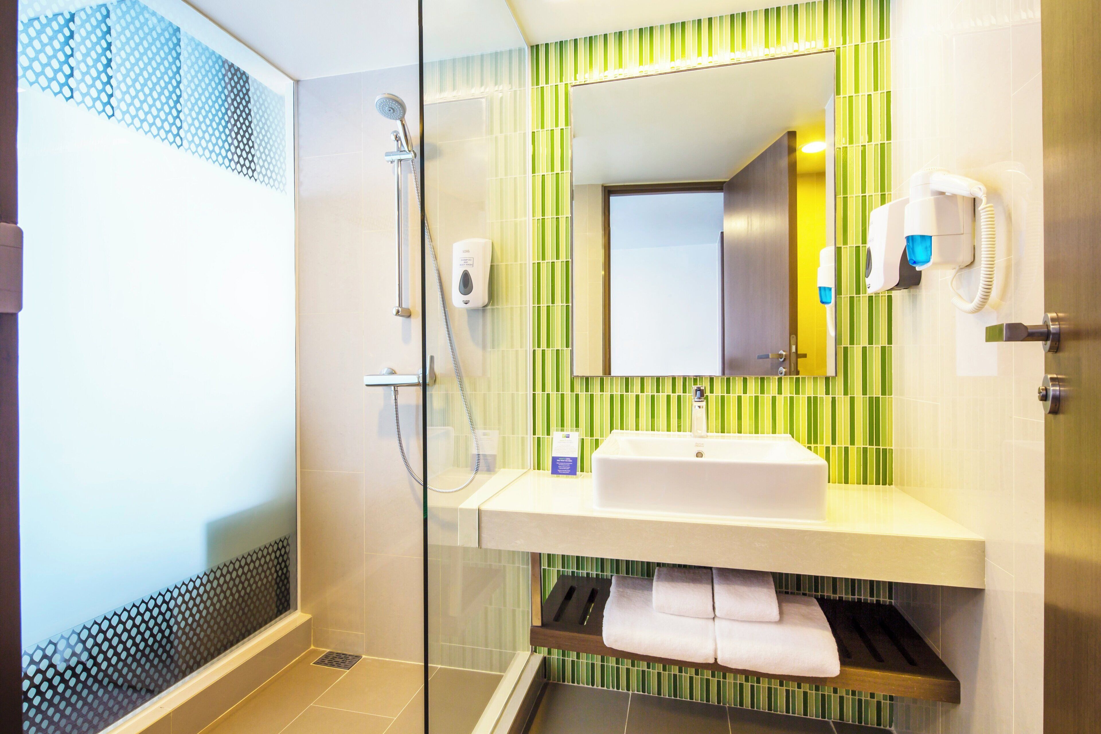 Un baño moderno con ducha de vidrio, lavamanos blanco y salpicadero de azulejos a rayas verdes.