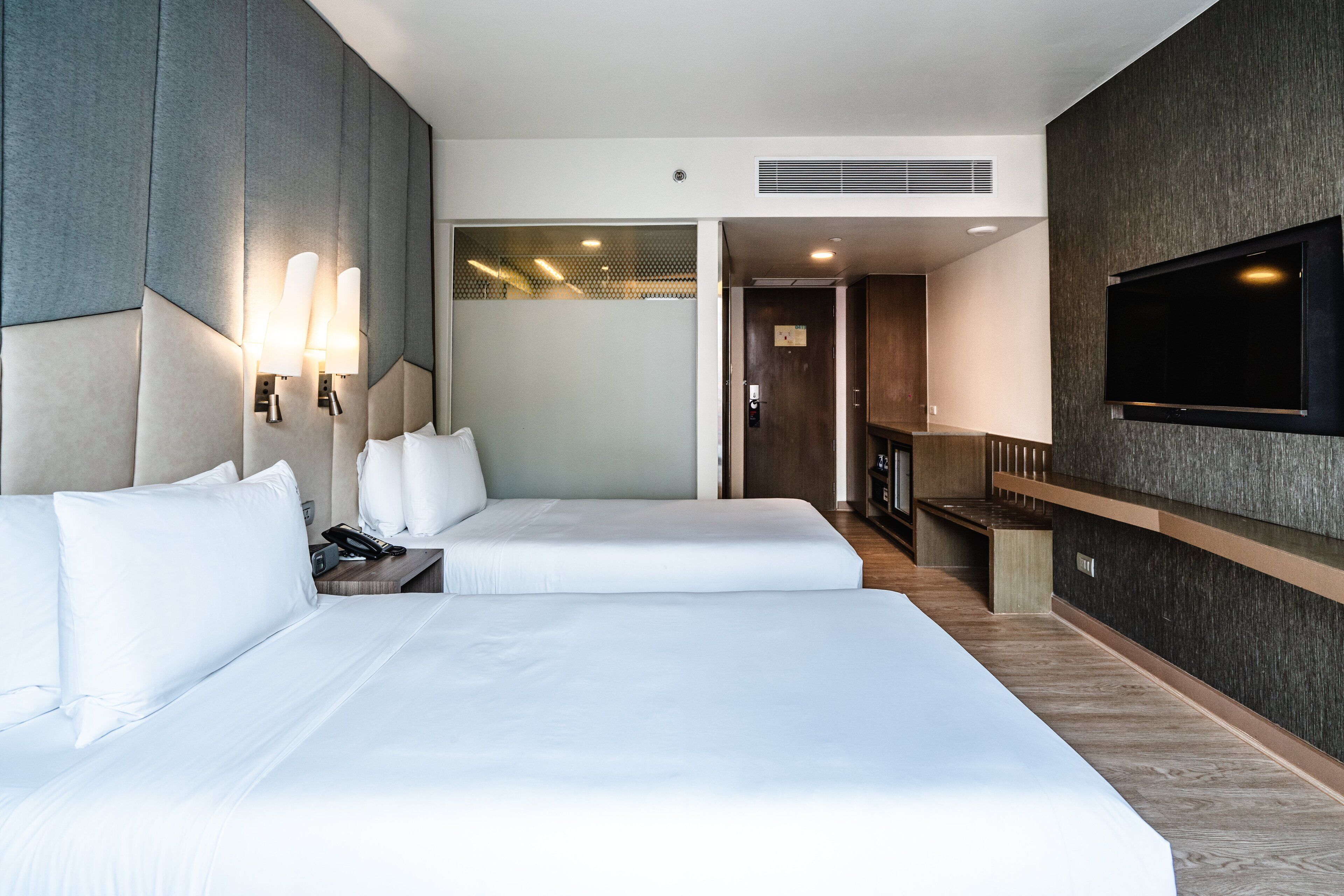 Une chambre d’hôtel moderne équipée de deux lits, d’un téléviseur à écran plat et d’un petit coin salon.