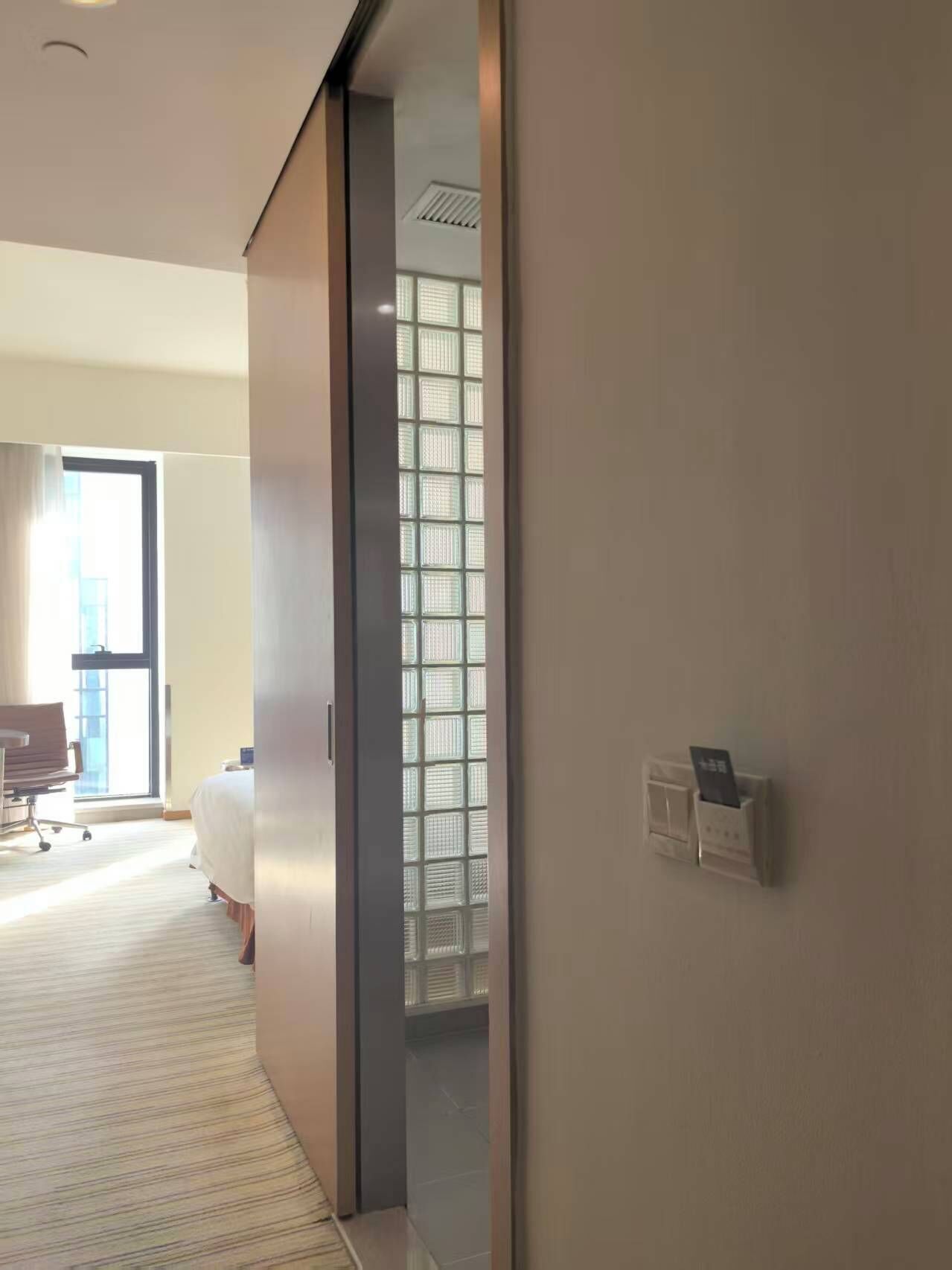 A hotel room with a sliding door, a bed, a desk, and a window with blinds.