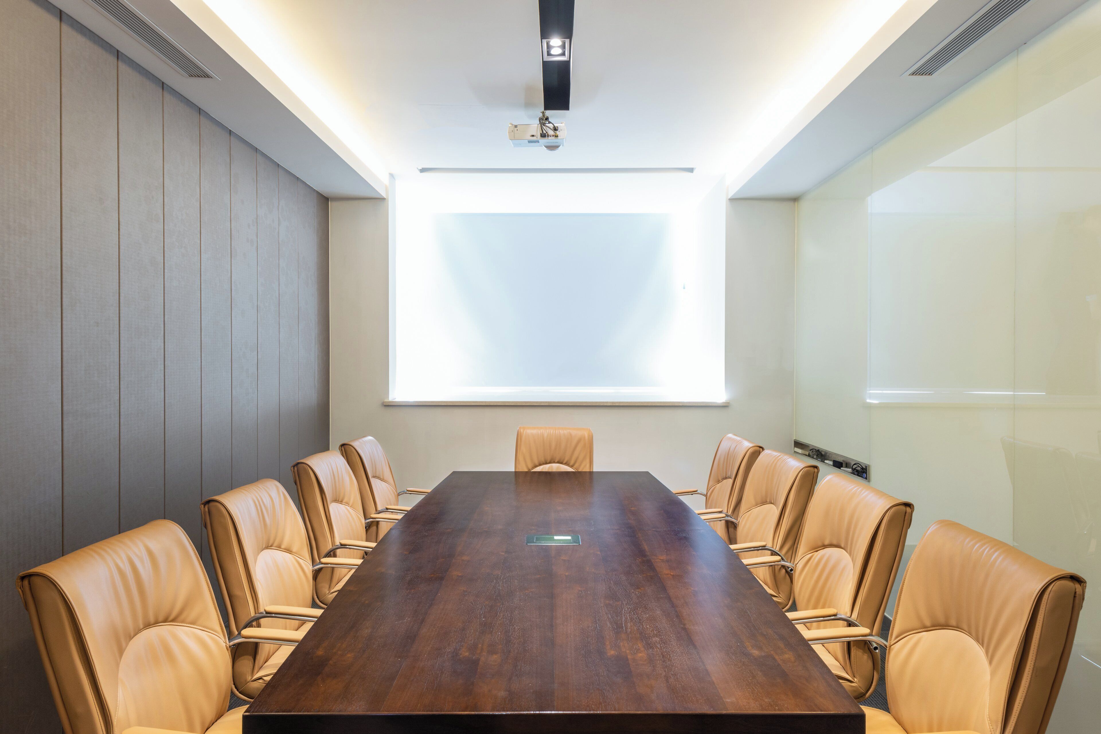 Un salón de conferencias con una larga mesa y sillas de cuero, una pantalla de proyector y un ventanal.