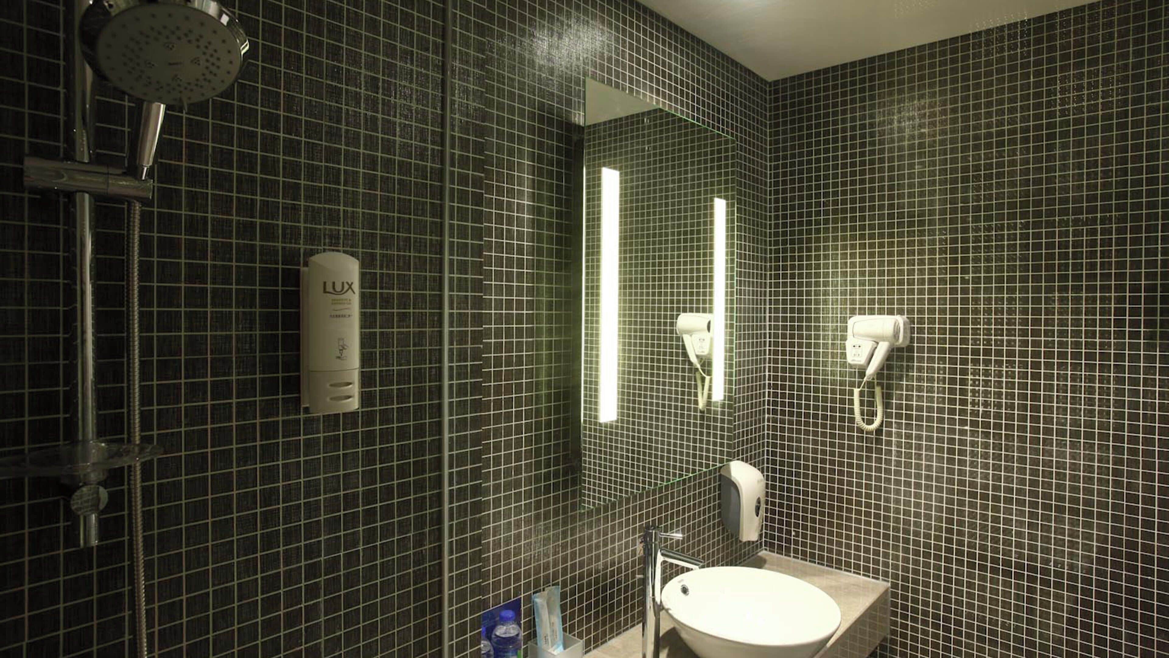 A bathroom with a shower, a sink, and a hairdryer mounted on the wall.