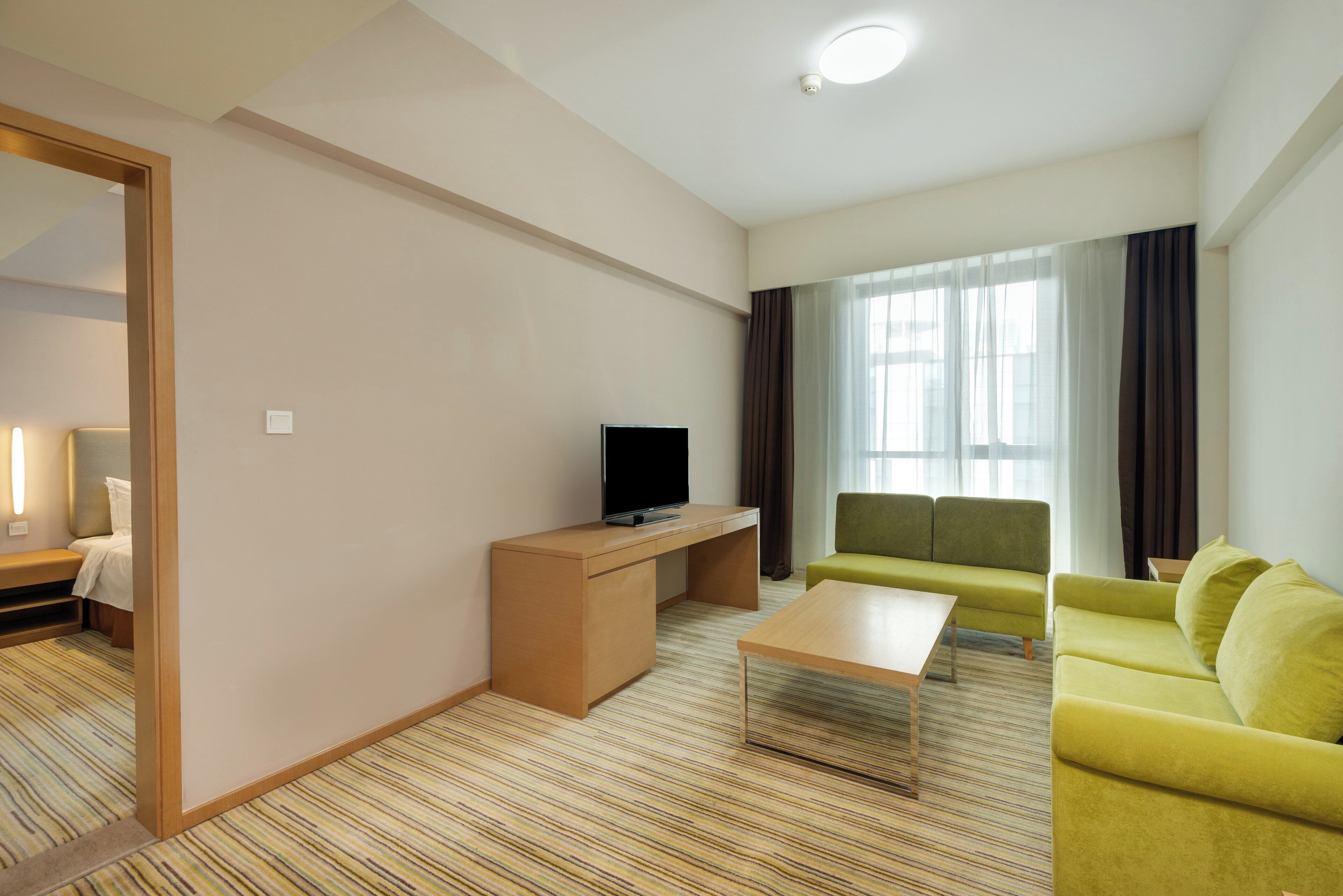 A modern hotel room with a sofa, a television, a desk, and a bed.
