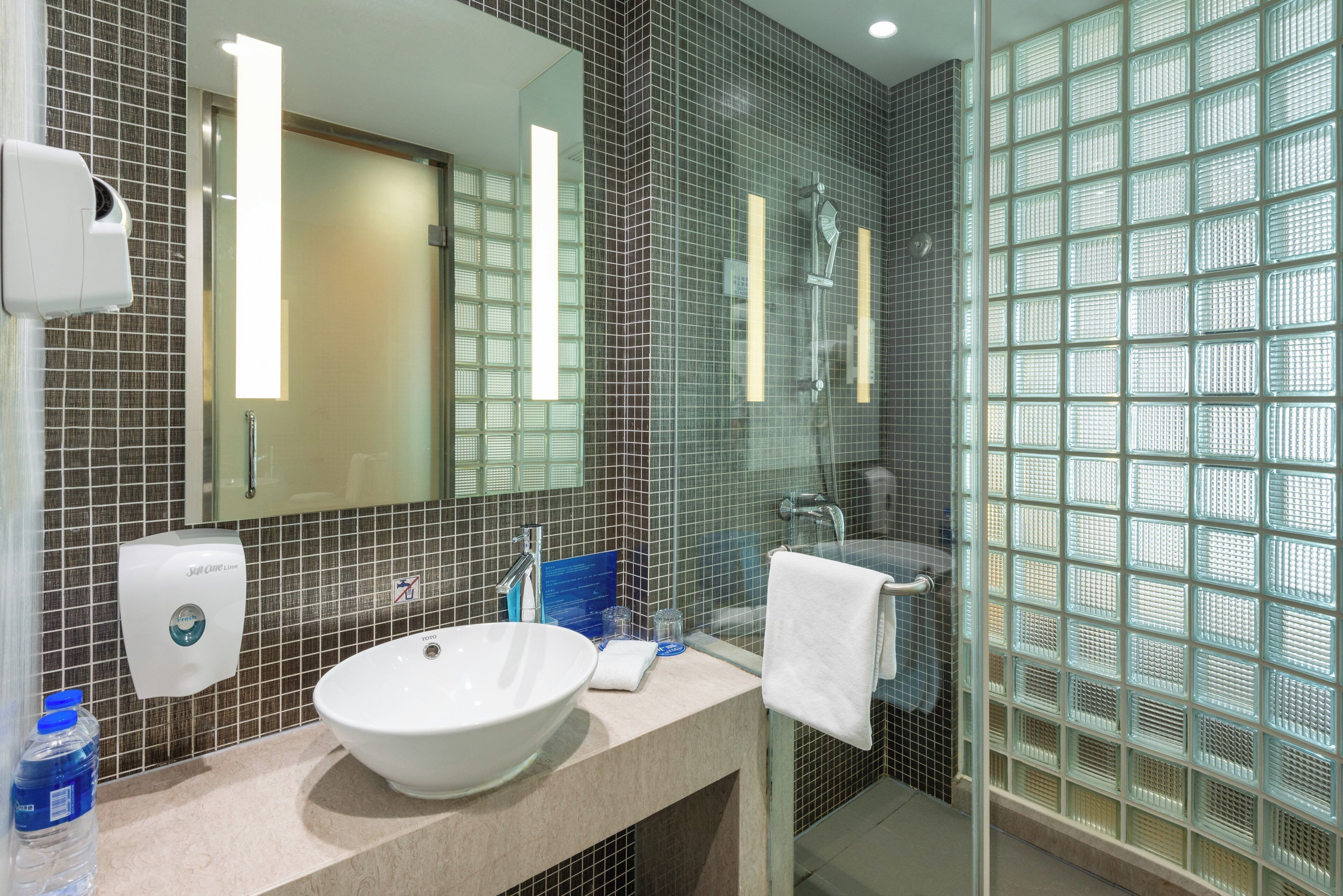 A modern bathroom with a large mirror, a white sink, a glass shower enclosure, and a hand dryer.