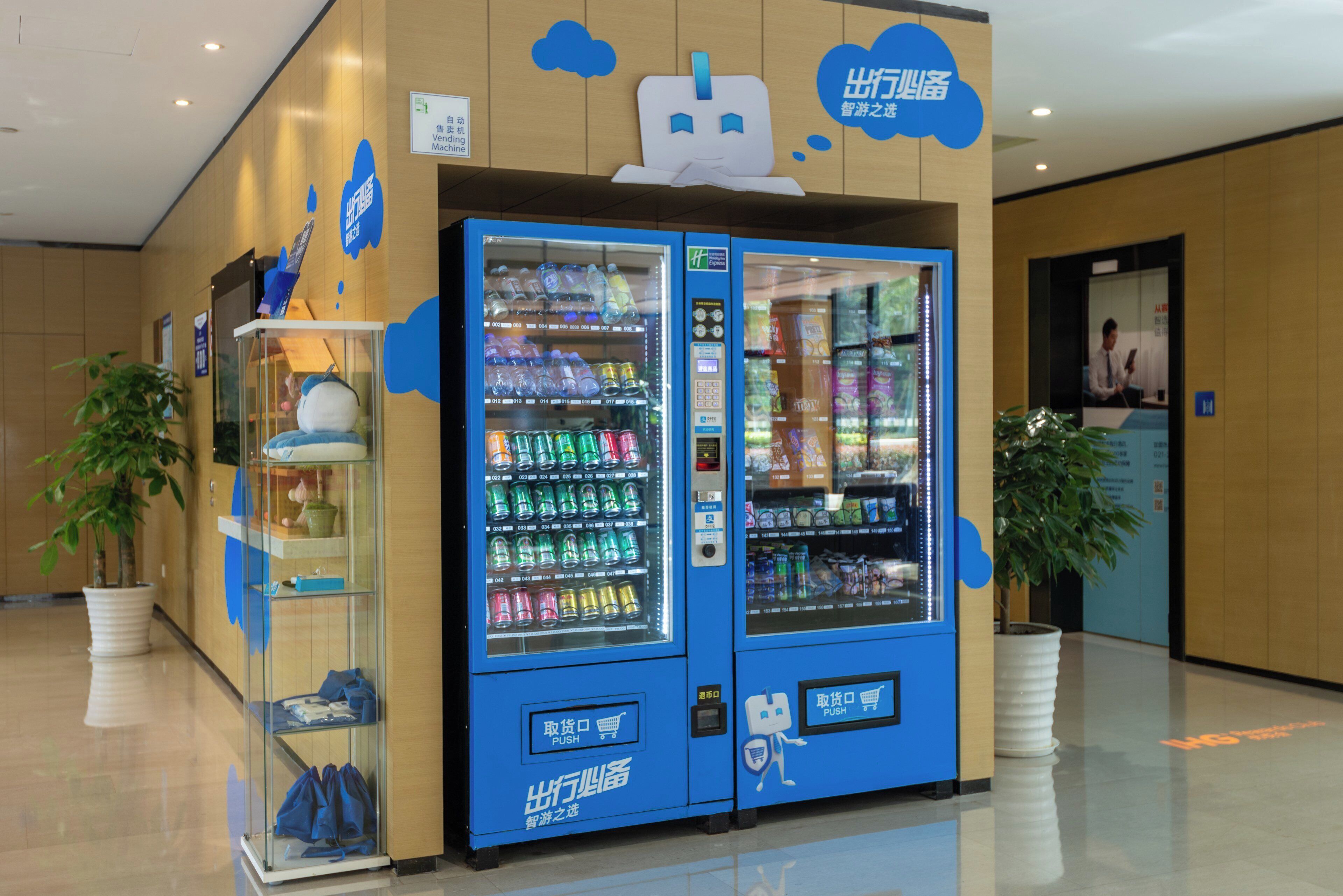 Un distributeur automatique proposant une variété de boissons et d’en-cas, situé dans un espace intérieur bien éclairé, agrémenté de lambris en bois et de plantes en pot.