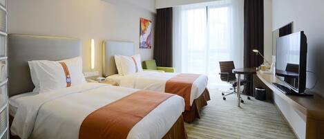 A hotel room with two beds, a desk, a chair, a television, and a large window.