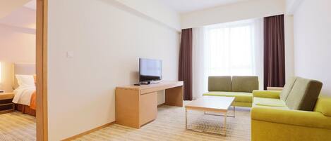A hotel room with a bed, a TV on a desk, a sofa, and a window with curtains.