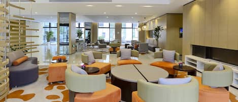 A spacious lobby with modern seating, a large TV screen, and large windows offering views of the outside.