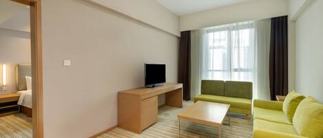 Ein modernes Hotelzimmer mit einem Bett, einem Schreibtisch mit Flachbildfernseher, einem grünen Sofa und einem Couchtisch.