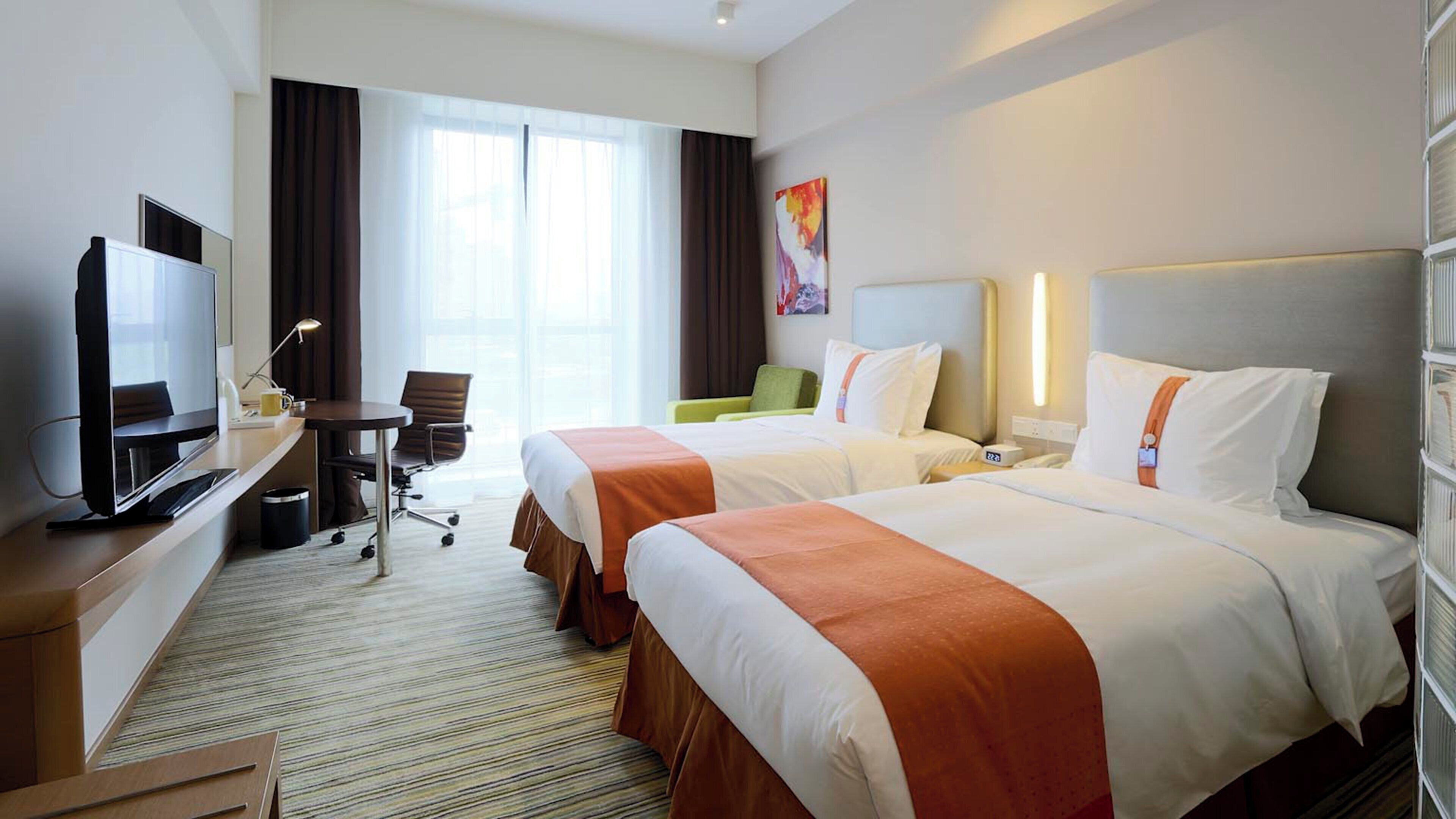 A hotel room with two beds, a desk with a TV, a chair, and a window with curtains.