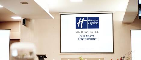 A conference room with a large screen displaying the Holiday Inn Express logo and the text 'AN IHG HOTEL SURABAYA CENTERPOINT.'