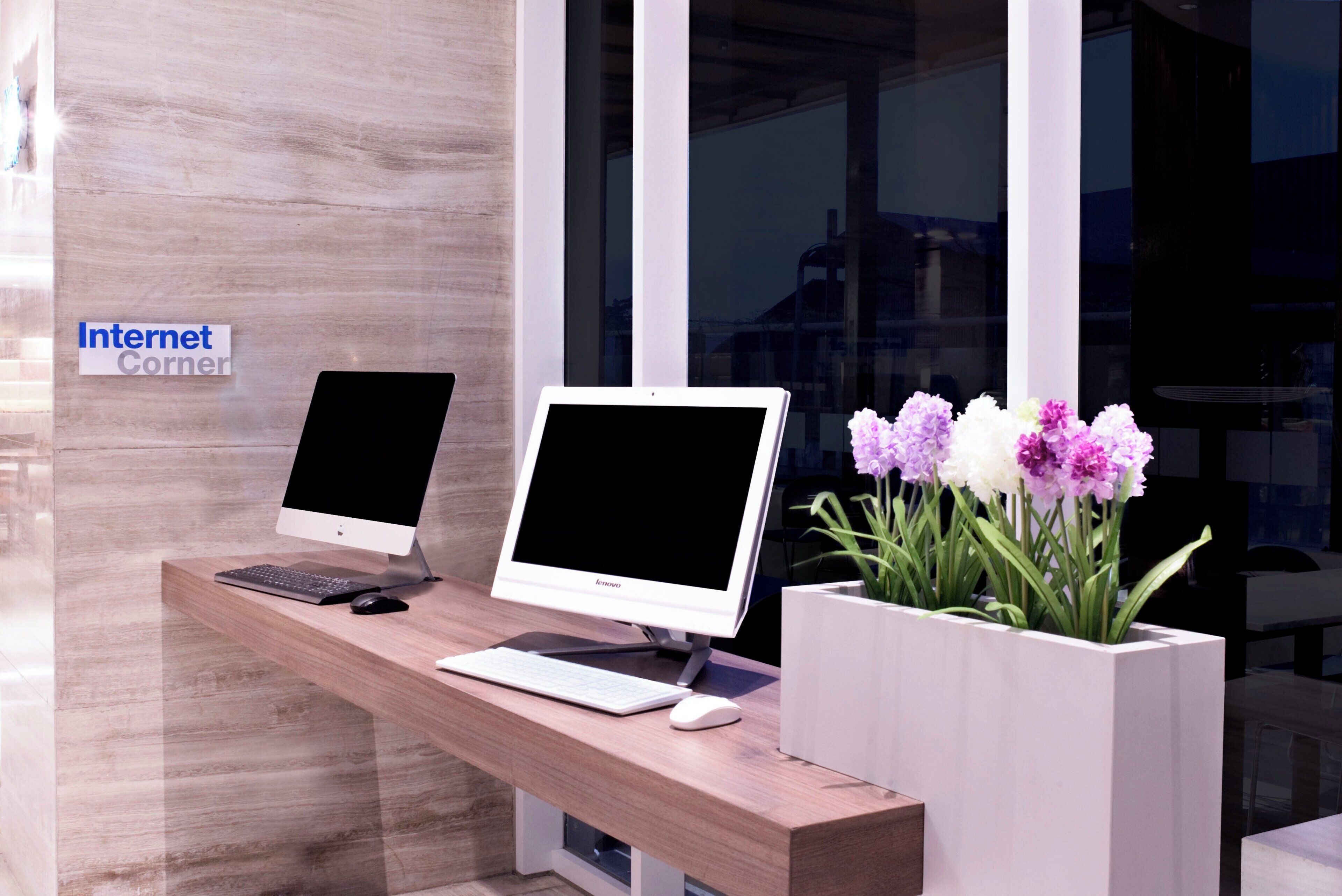 Un mostrador de recepción con dos monitores de computadora, un teclado, un ratón y un florero con flores.