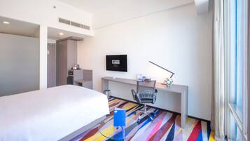A hotel room with a bed, a desk, a chair, a television, and a colorful carpet.